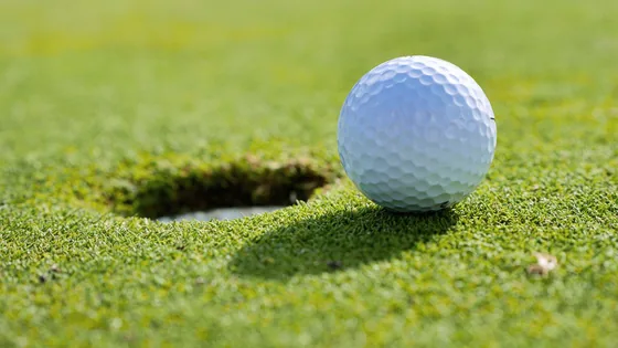 A golf ball at rest on a green a few inches from the hole, seen close in.