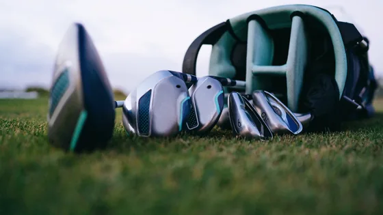 A driver, a set of clubs and an open bag lying on mown turf, seen from ground level under a grey evening sky.